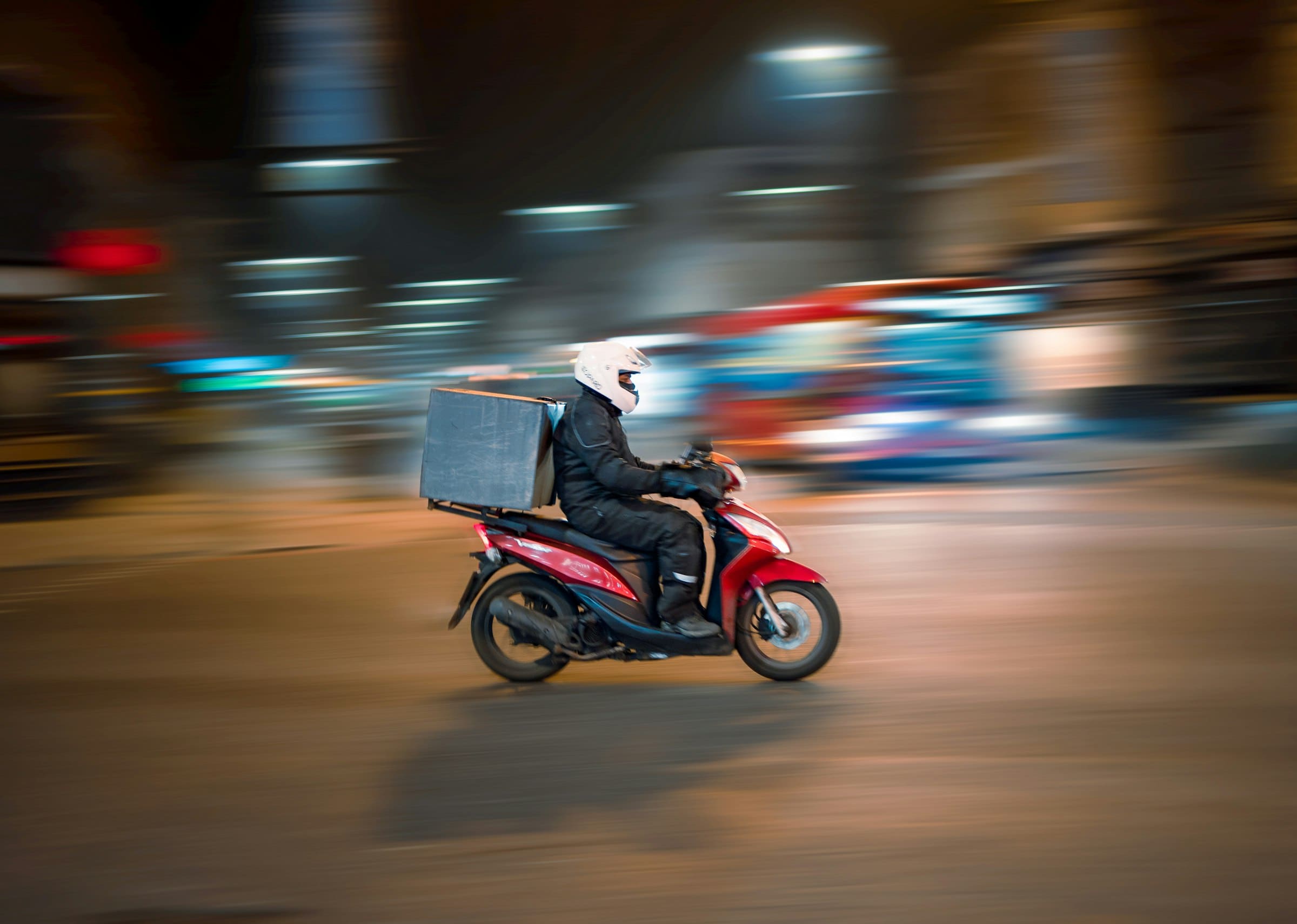 A courier riding through a city at night, streetlights blurred behind