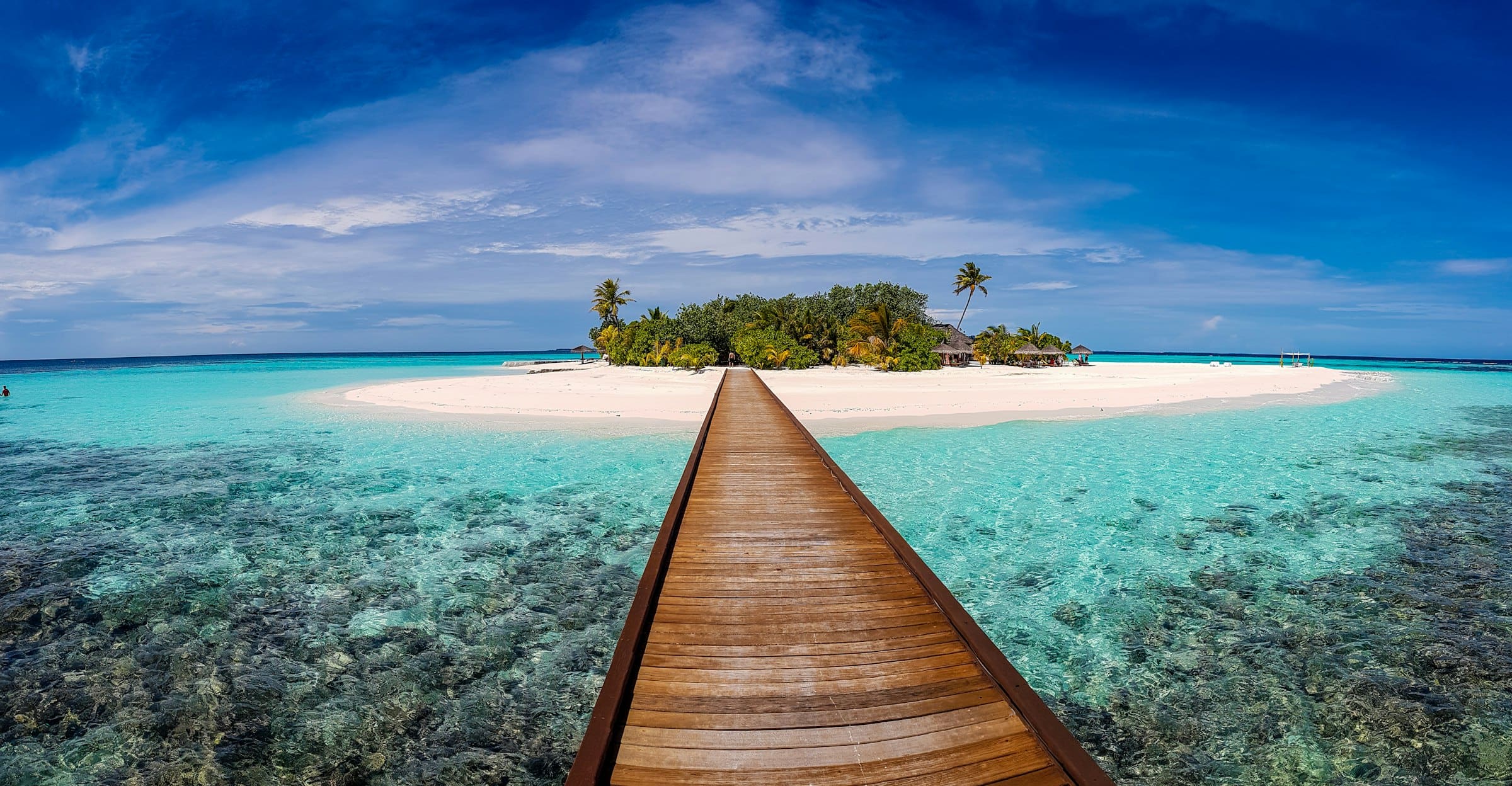 A wooden boardwalk stretching over turquoise water towards a small island