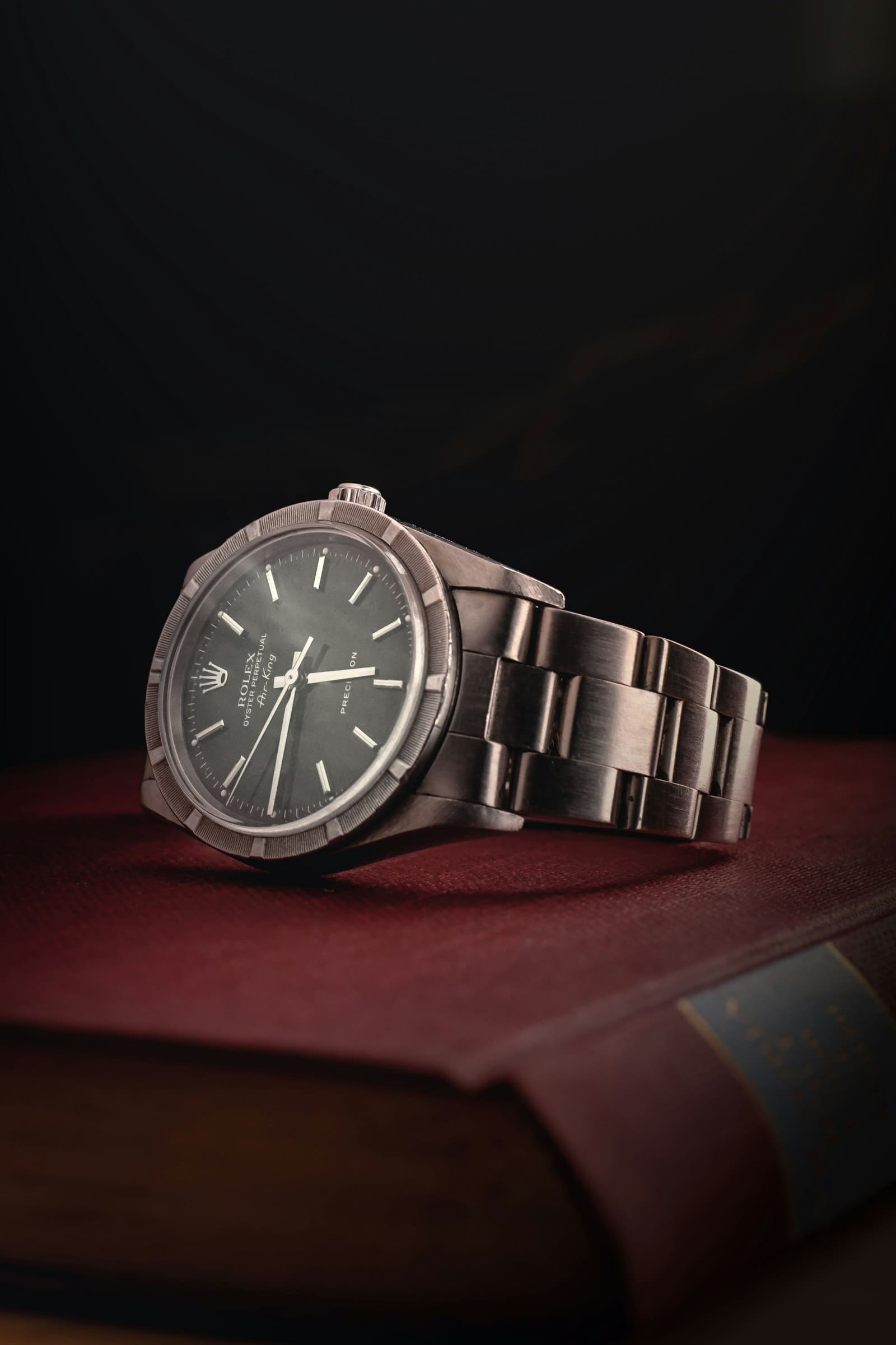 A steel wristwatch resting on a leather-bound book against a dark background